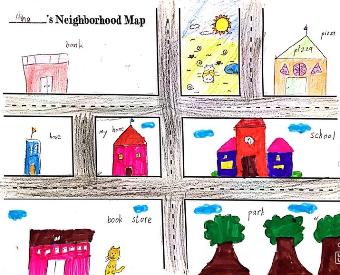 A second grade student uses a colorful neighborhood map with a key and compass rose to answer map-reading questions