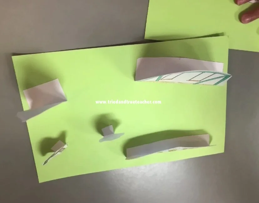 First grade worksheet featuring a pop-up park with a swing set, slide, and trees with animals