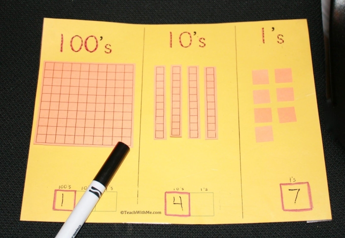 Second grade student using a place value mat to practice three-digit numbers in a geography-themed worksheet